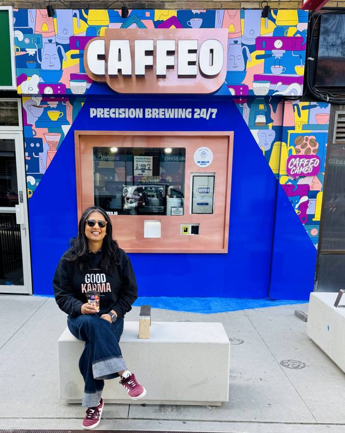 Nida in a Good Karma hoodie outside the colorful Caffeo robotic coffee kiosk
